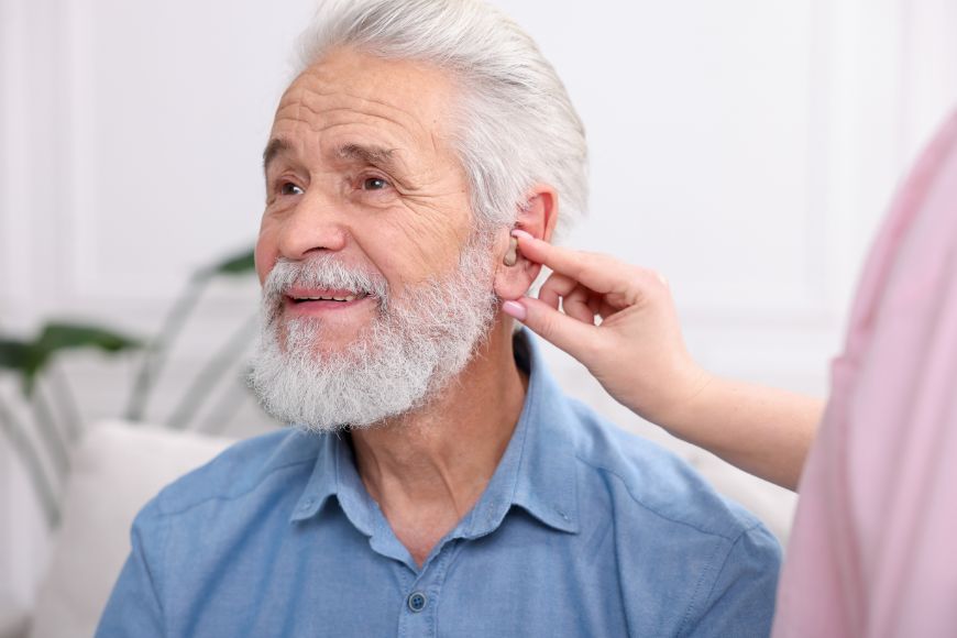 Caregiver adjusting an older man’s hearing aid